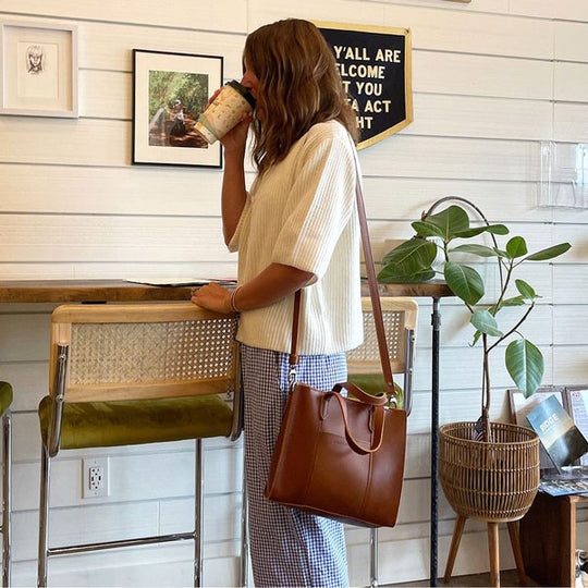 A person holding a coffee cup with a Lola Crossbody Bag.