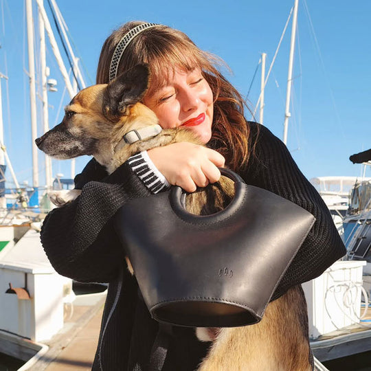A person standing on a dock holding a dog in a Milan Leather Handbag.
