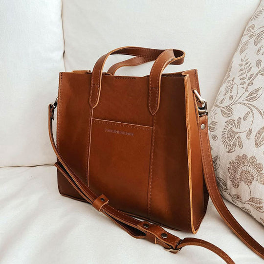 A Lola Crossbody Tote in Honey sitting on a couch.