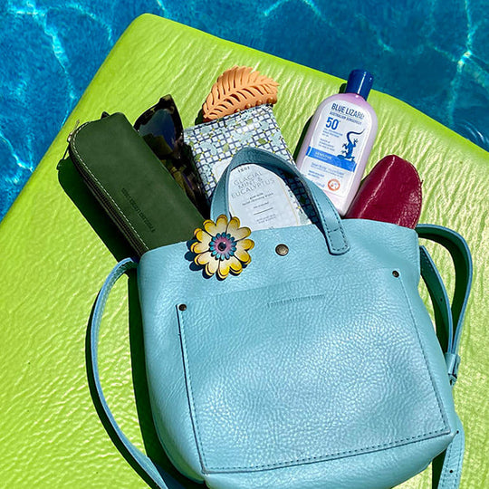 A light blue pebbled leather handbag sitting poolside with accessories inside