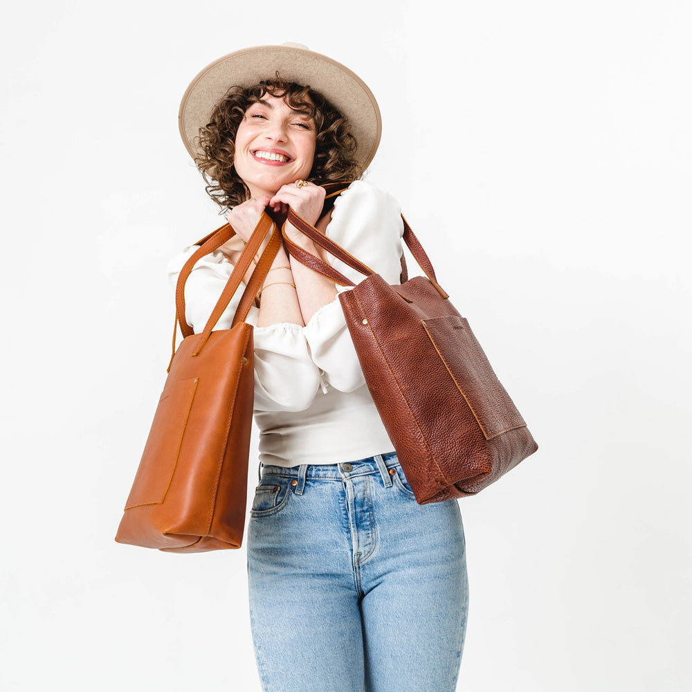 Smiling woman in a hat holding two brown leather tote bags