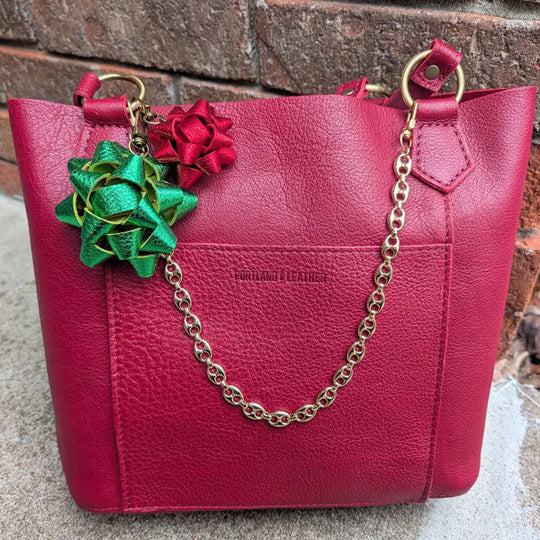 Red handbag with floral keychains and a gold chain on a stone surface.