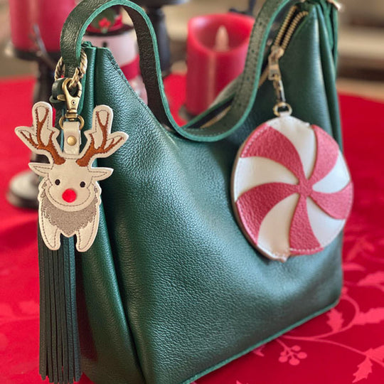 Green handbag with reindeer charm and peppermint candy charm on a red table.
