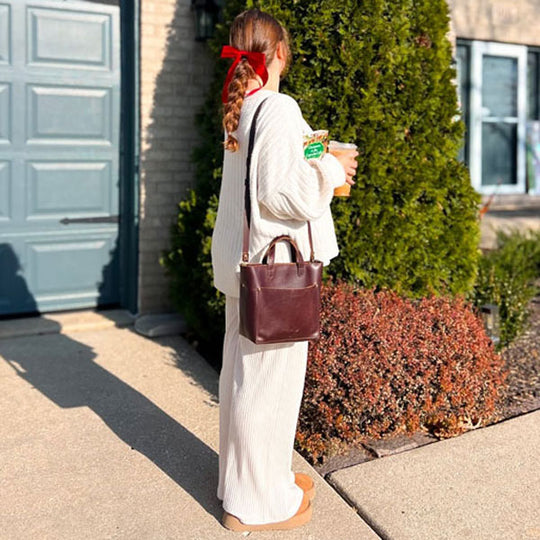 Person in a white outfit with a brown leather bag standing outside a house