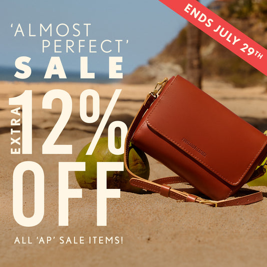 A brown leather crossbody bag on a sandy beach