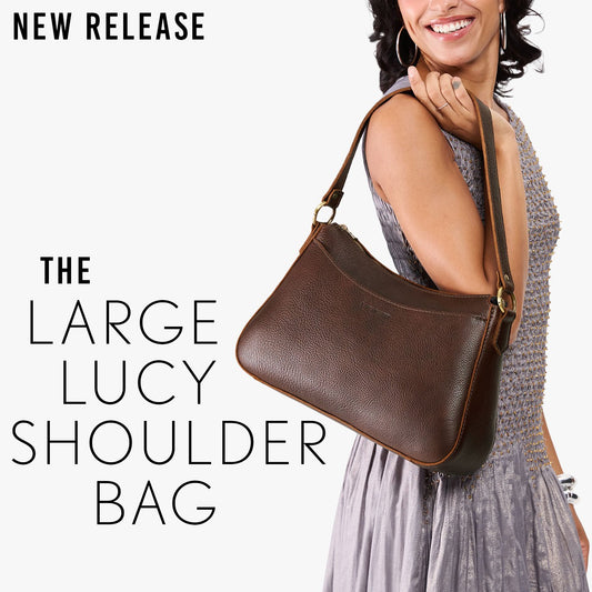 A model holding a large leather shoulder bag with a wide strap. The image includes promotional text reading 'NEW RELEASE' and 'THE LARGE LUCY SHOULDER BAG' on a white background.