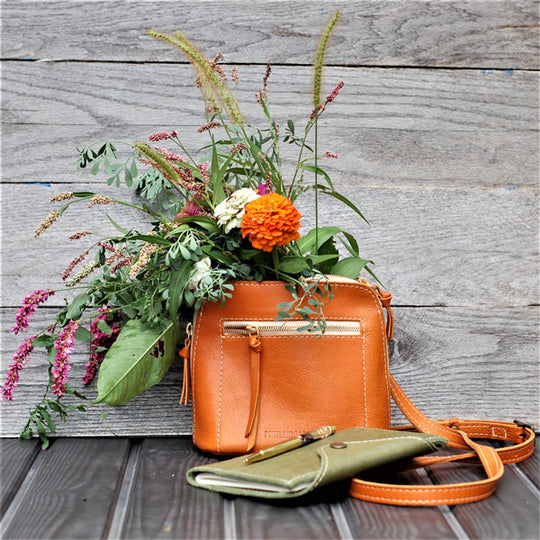 Luna Crossbody with a floral arrangement on a wooden surface