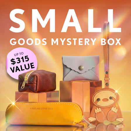Promotional graphic for a 'Small Goods Mystery Box' featuring a collection of pouches, wallets, and small goods. Set against a sparkly background with a pink badge indicating up to $315 value.