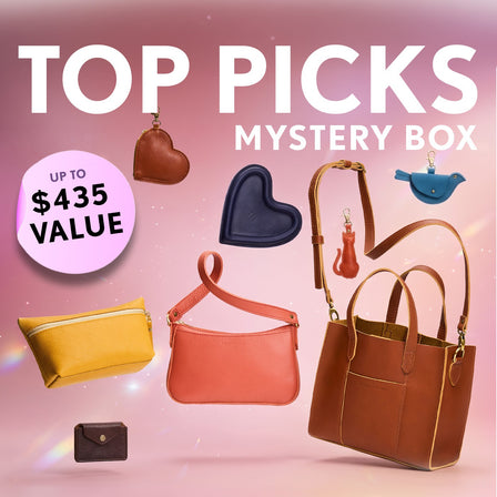 Promotional graphic for a 'Top Picks Mystery Box' featuring a collection of bags, wallets, and small goods. Set against a sparkly background with a pink badge indicating up to $435 value.