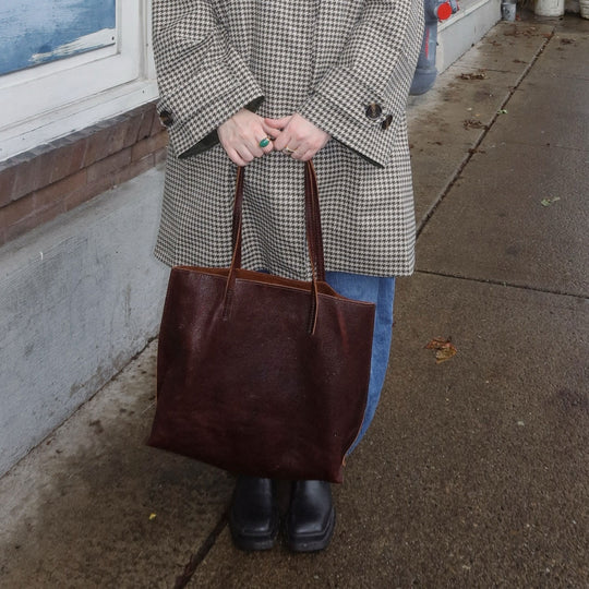person holding a August Tote bag in a checkered jacket and jeans