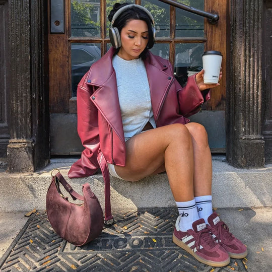 Person sitting on steps holding coffee next to a PLG bag