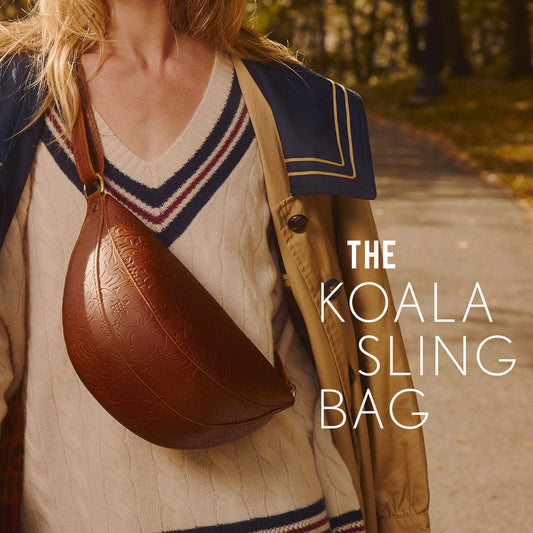A woman outdoors wearing a brown embossed leather Koala Sling Bag across her torso. White text on the right reads 'THE KOALA SLING BAG'.