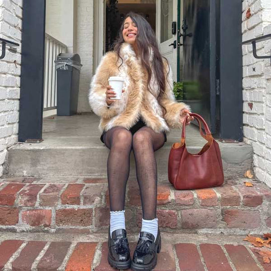 Woman sitting on steps holding a coffee cup and leather shoulder bag