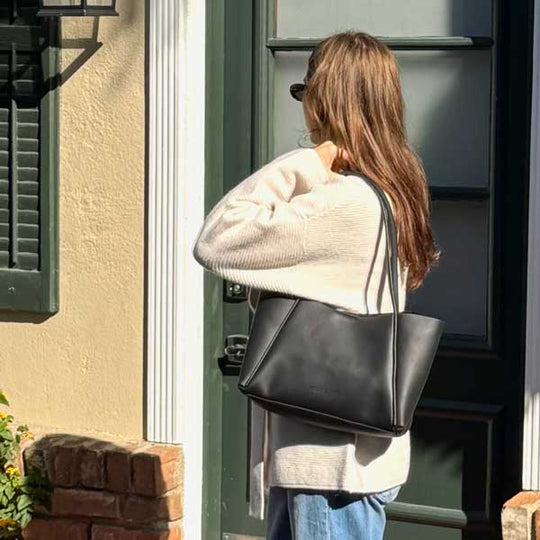 Woman standing in front of green door carrying a dark leather tote bag