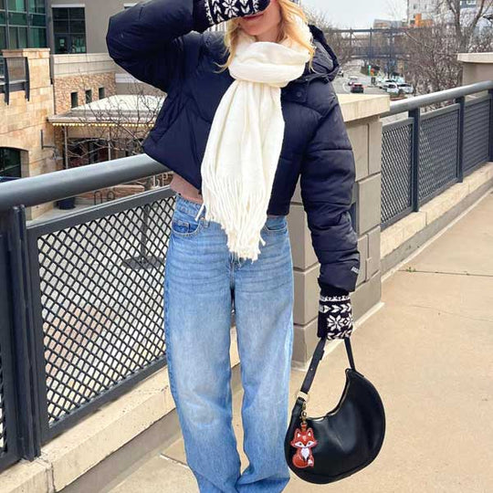 Woman wearing a white scarf and wintery jacket holding a dark leather bag with a fox keychain accessory