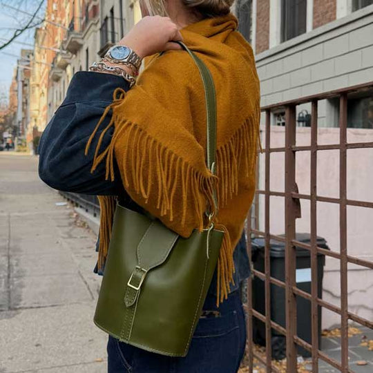 Person wearing a mustard yellow fringed jacket with a green bag on an urban street.