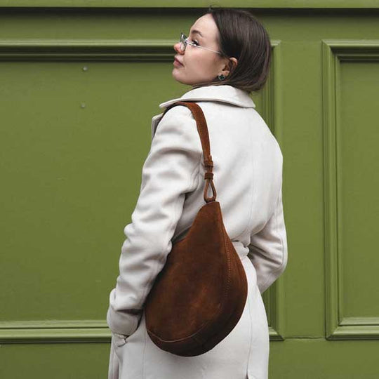 Woman in a white coat with a brown leather bag against a green wall