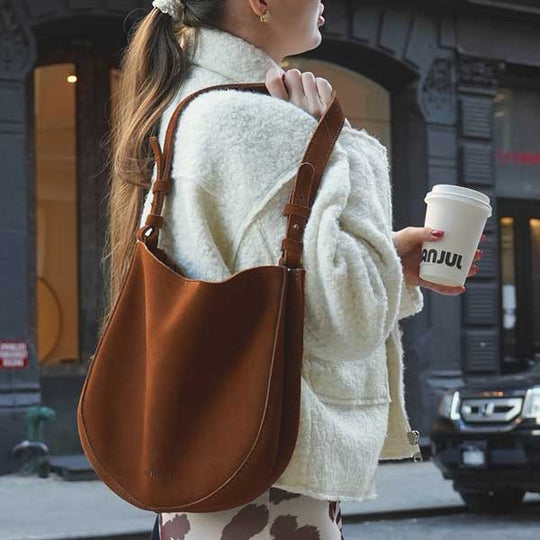 Woman holding coffee cup and carrying leather shoulder bag