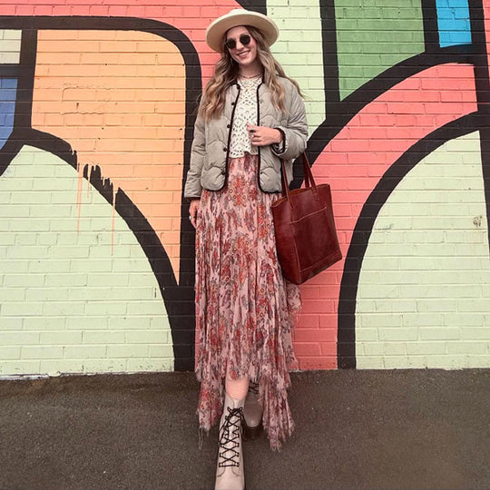 Woman standing in front of a colorful mural wearing a floral dress and carrying a Crossbody Tote