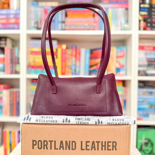 Amelie Shoulder Bag on a box with 'Portland Leather' branding in front of a bookshelf.