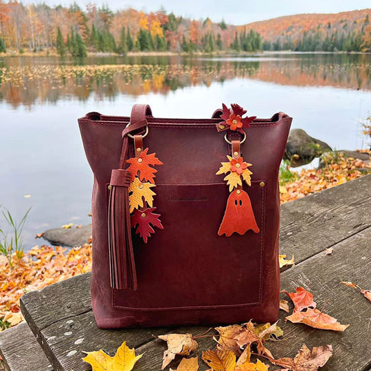 Crossbody Tote with autumn leaf decorations on a wooden bench by a lake.