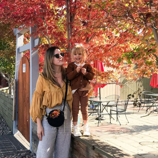 Woman and child standing under a tree with autumn leaves, with outdoor furniture in the background wearing a Circle Bag