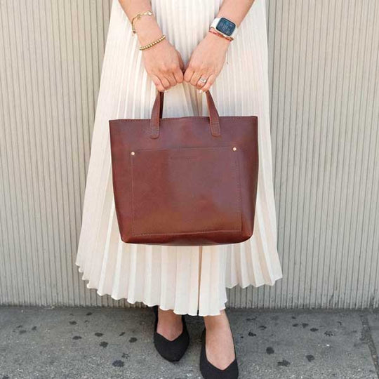 Person holding a brown leather tote bag against a neutral background