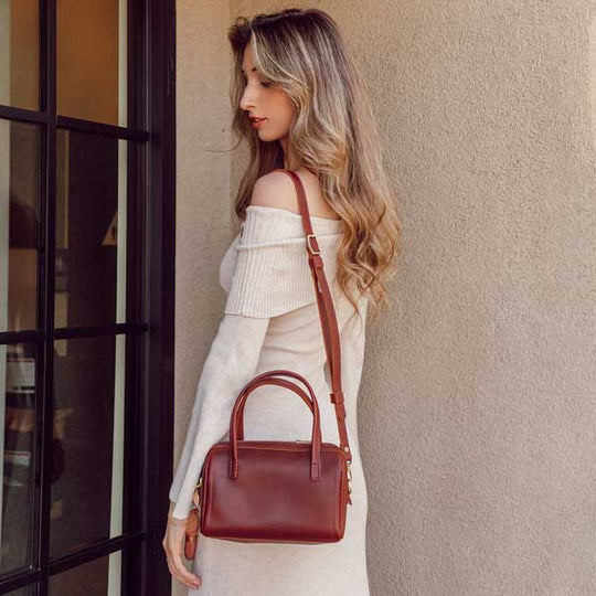 Woman holding a red handbag against a neutral wall