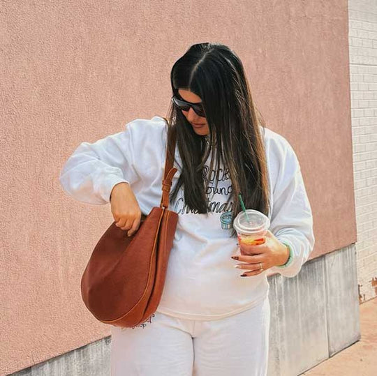 Woman in white outfit with brown leather bag and colorful drink against a pink wall