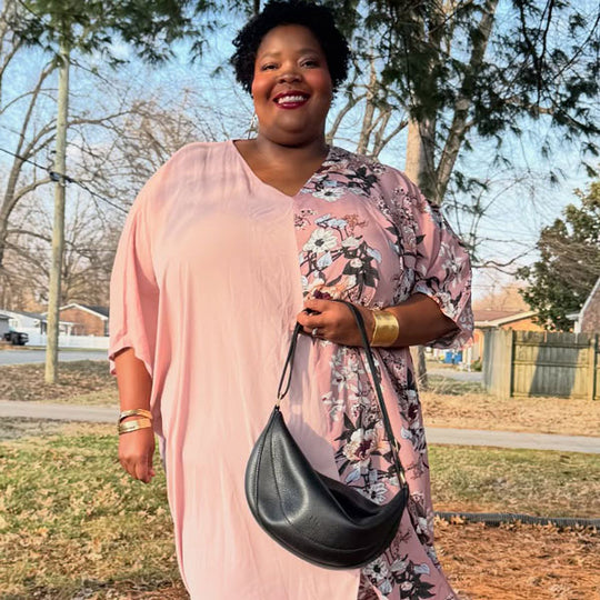Person in a pink dress with floral pattern holding a black Koala Sling Bag outdoors.