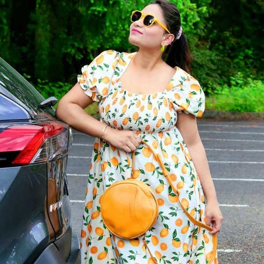Person in a sundress with lemons on it, standing next to a car holding a yellow circle bag