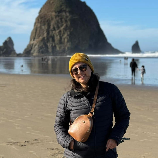 Person standing on a beach with a Sydney Sling Bag with a large rock formation in the background