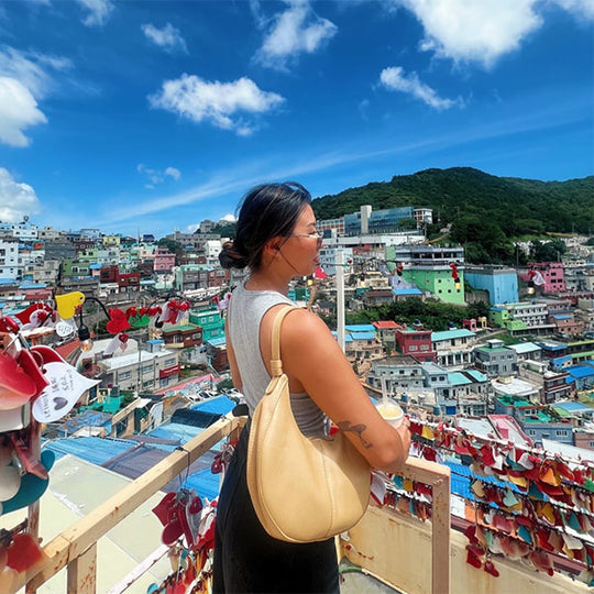 Women wearing a light brown bag with a colorful city in the background