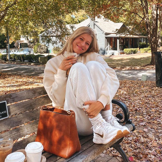 A person sitting on a bench with their knees up next to a Triangle Shoulder Bag