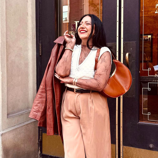 Person standing in front of a doorway carrying a jacket and the Nora Shoulder Bag