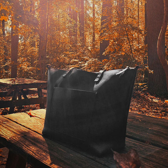 A leather Tote sitting on a rustic picnic table with a glowing fall background