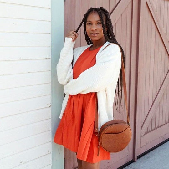 A person holding one of their braids and carrying a Circle Crossbody Bag in Meadow.