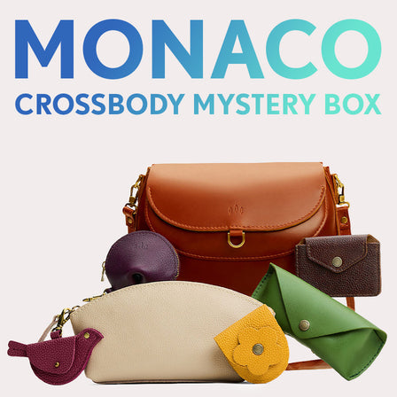 Monaco Crossbody in Nutmeg next to Utility Bag, Taco Tassel Pouch, Daisy Plus Wallet, and a Leather Wrap Journal. Text reads "Monaco Crossbody Mystery Box"