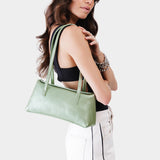 Beetle | Woman holding a shiny green leather bowler bag against a white background
