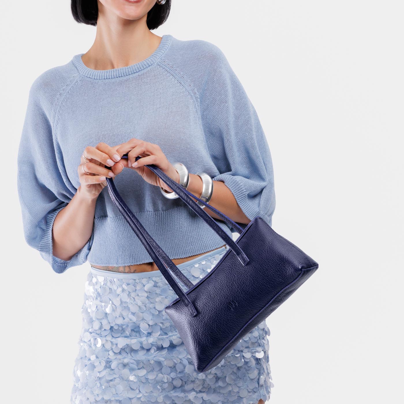 Cobalt | Woman holding a dark blue leather bowler bag against a white background
