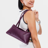 Plum | Woman wearing a purple leather bowler bag against a white background