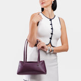 Plum | Woman wearing a purple leather bowler bag against a white background