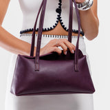 Plum | Woman opening a purple leather bowler bag against a white background