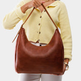 Nutmeg Large | Model holding u-shaped, flat-bottomed leather shoulder bag with adjustable strap