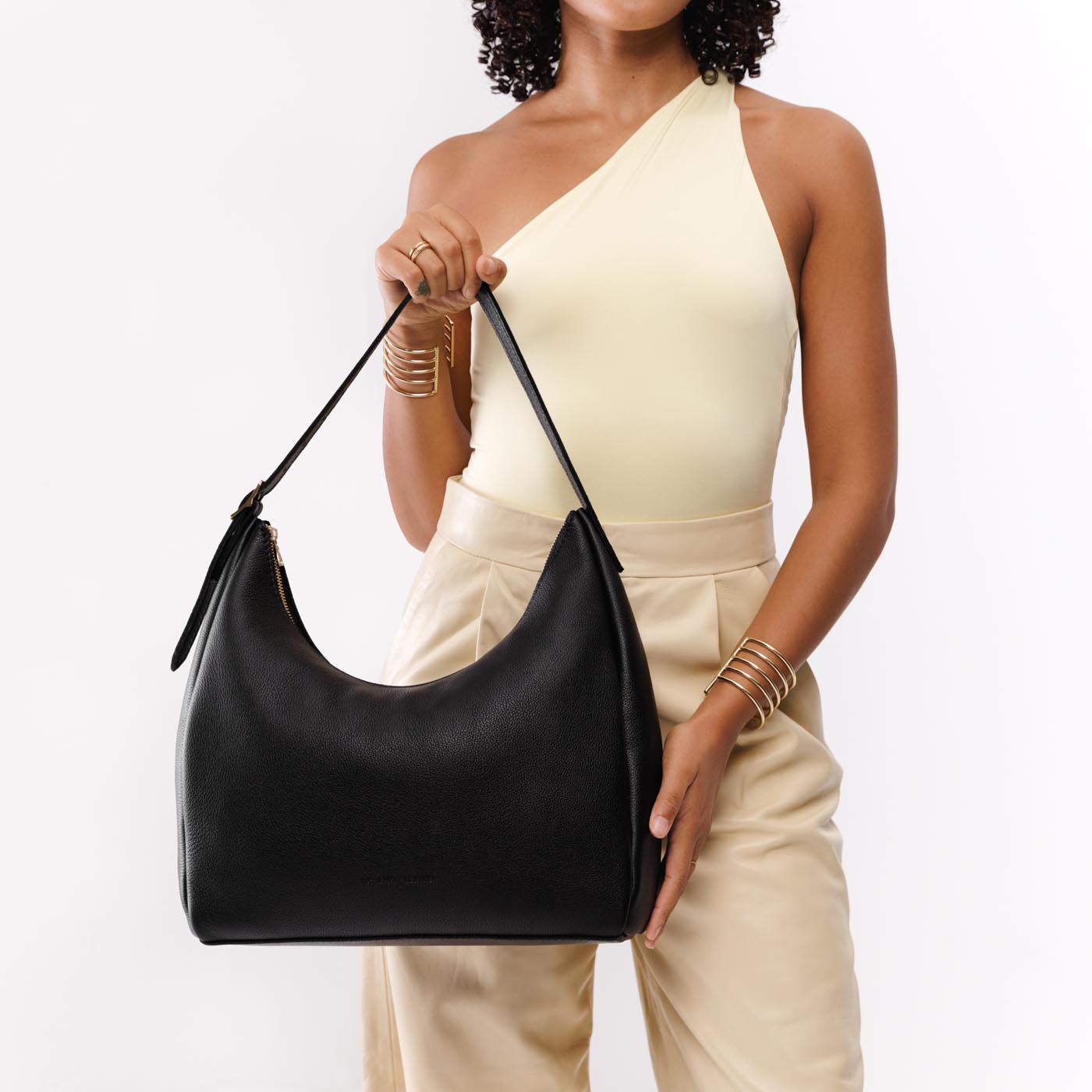 Pebbled--black*Large | Model holding u-shaped, flat-bottomed leather shoulder bag with adjustable strap
