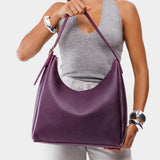 Plum Large | Model holding u-shaped, flat-bottomed leather shoulder bag with adjustable strap