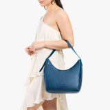 Caspian Medium | Model holding u-shaped, flat-bottomed leather shoulder bag with adjustable strap