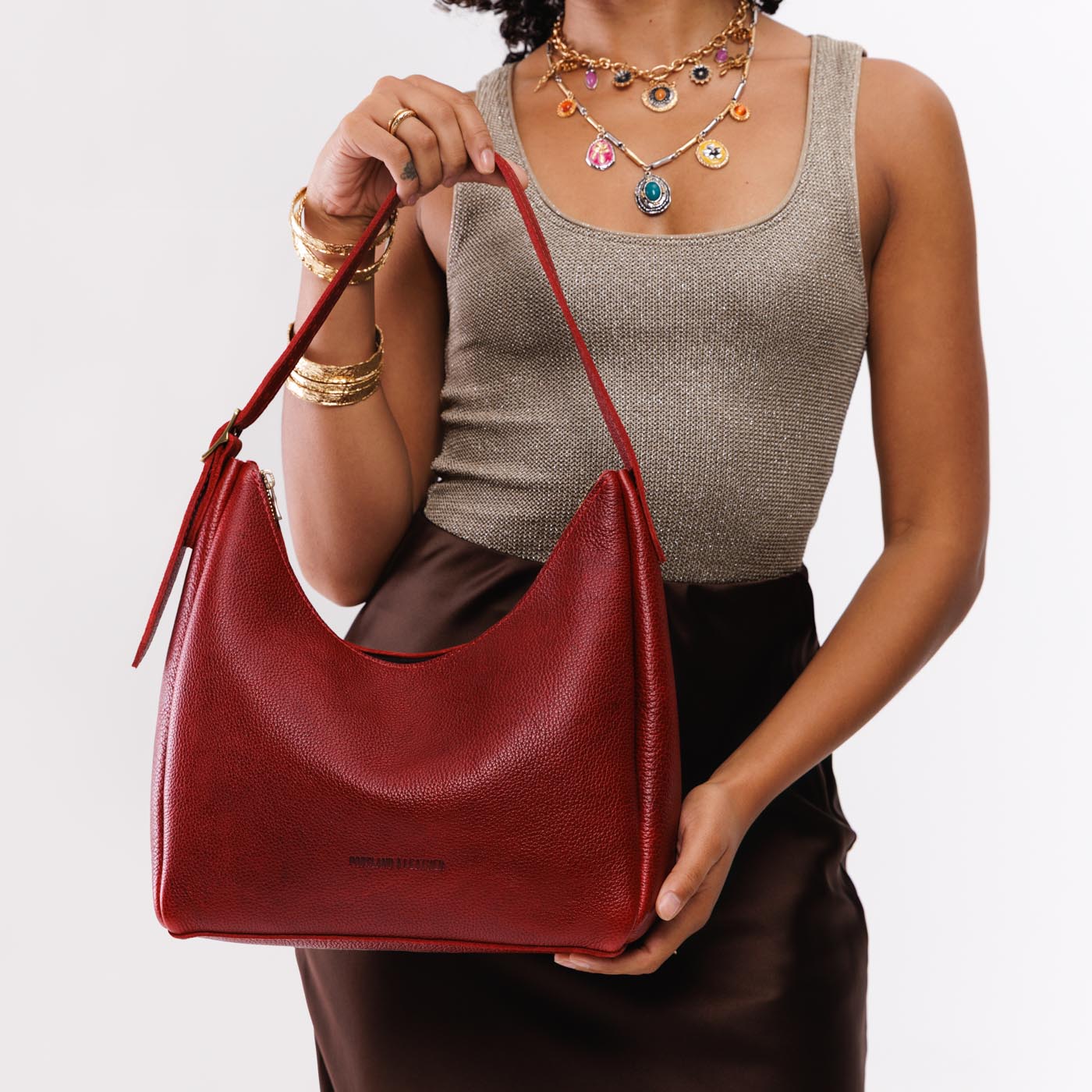 Chili Red*Medium | Model holding u-shaped, flat-bottomed leather shoulder bag with adjustable strap