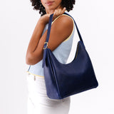 Med Aspen Shoulder Bag Mystery | Model holding u-shaped, flat-bottomed leather shoulder bag with adjustable strap