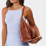 Nutmeg Medium | Model holding u-shaped, flat-bottomed leather shoulder bag with adjustable strap